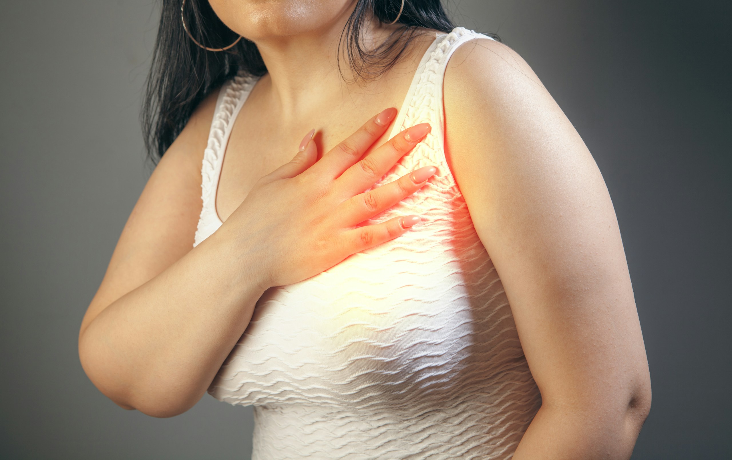 Woman suffering from chest pain on a gray background. Health care concept.